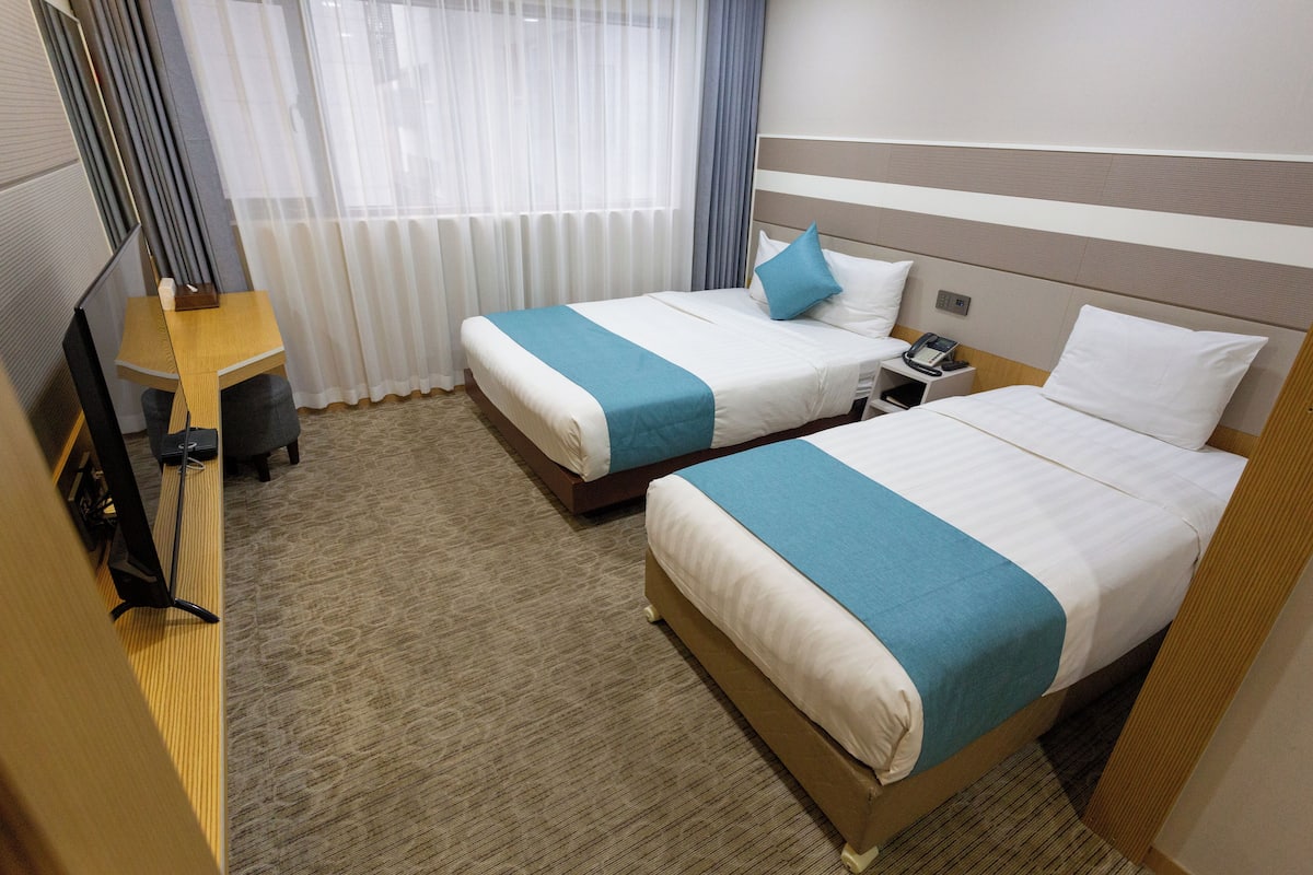Une chambre d’hôtel avec deux lits, un bureau et une télévision.
