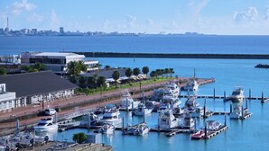 A marina with boats docked, a building with a sign, and a city skyline in the background. - Seaside Condominium Rana Chatan (Chatan)