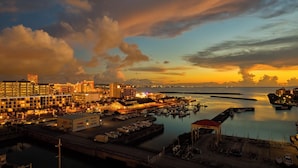 A coastal cityscape at sunset with illuminated buildings, a marina, and a bridge. - Seaside Condominium Rana Chatan (Chatan)