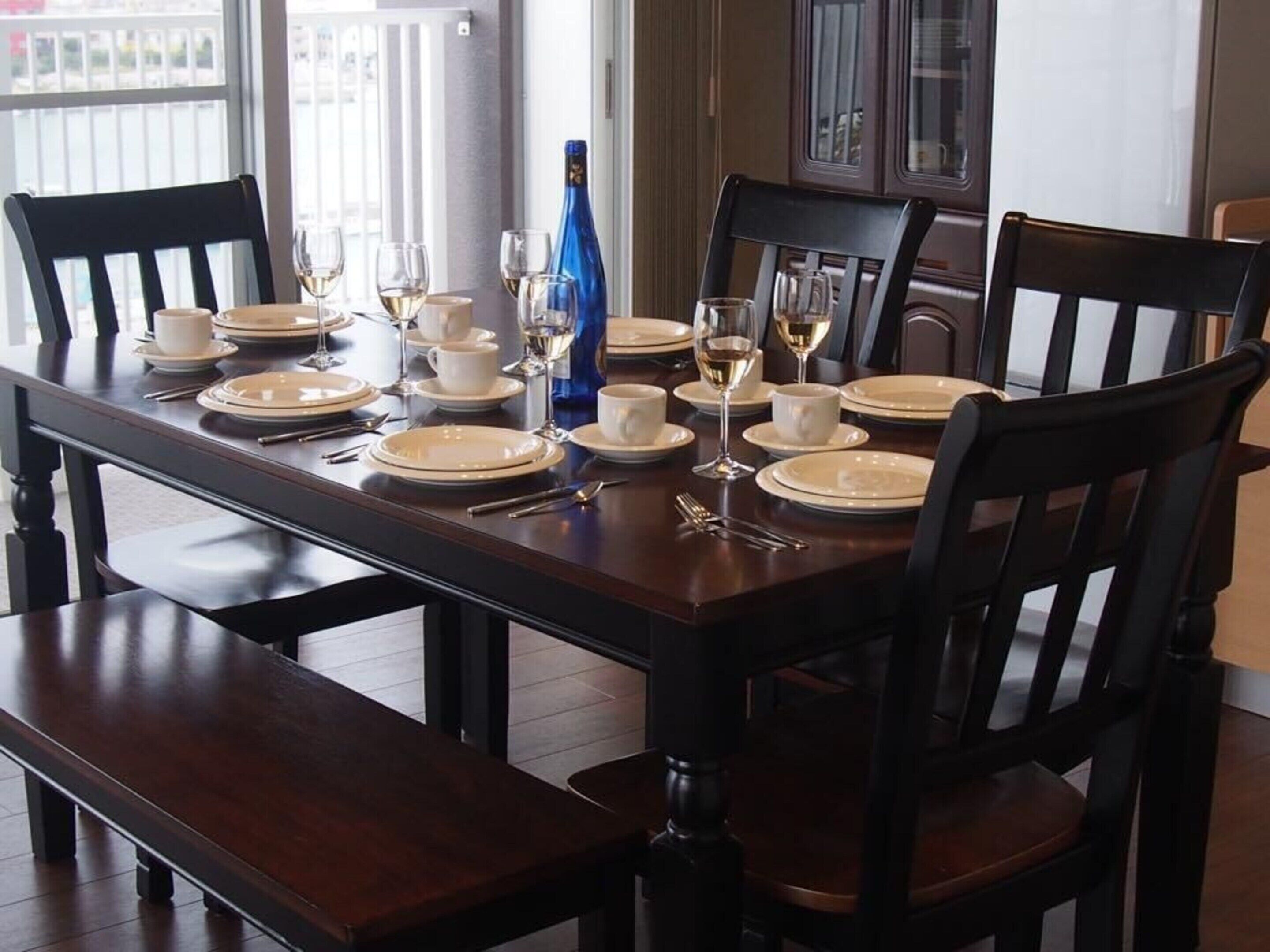 A dining table set for six with white plates, wine glasses, and a bottle of champagne.