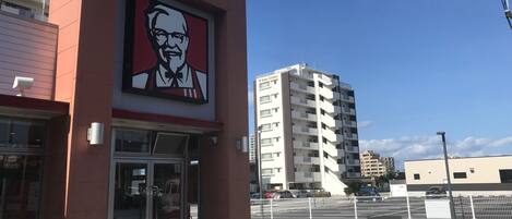 Un edificio con un llamativo logotipo de KFC en la fachada, una entrada de vidrio y un área de estacionamiento con cerramiento.