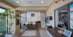 A reception area with a bench, a potted plant, a stone wall, and a sign welcoming to Okinawa. - Seaside Condominium Rana Chatan (Chatan)