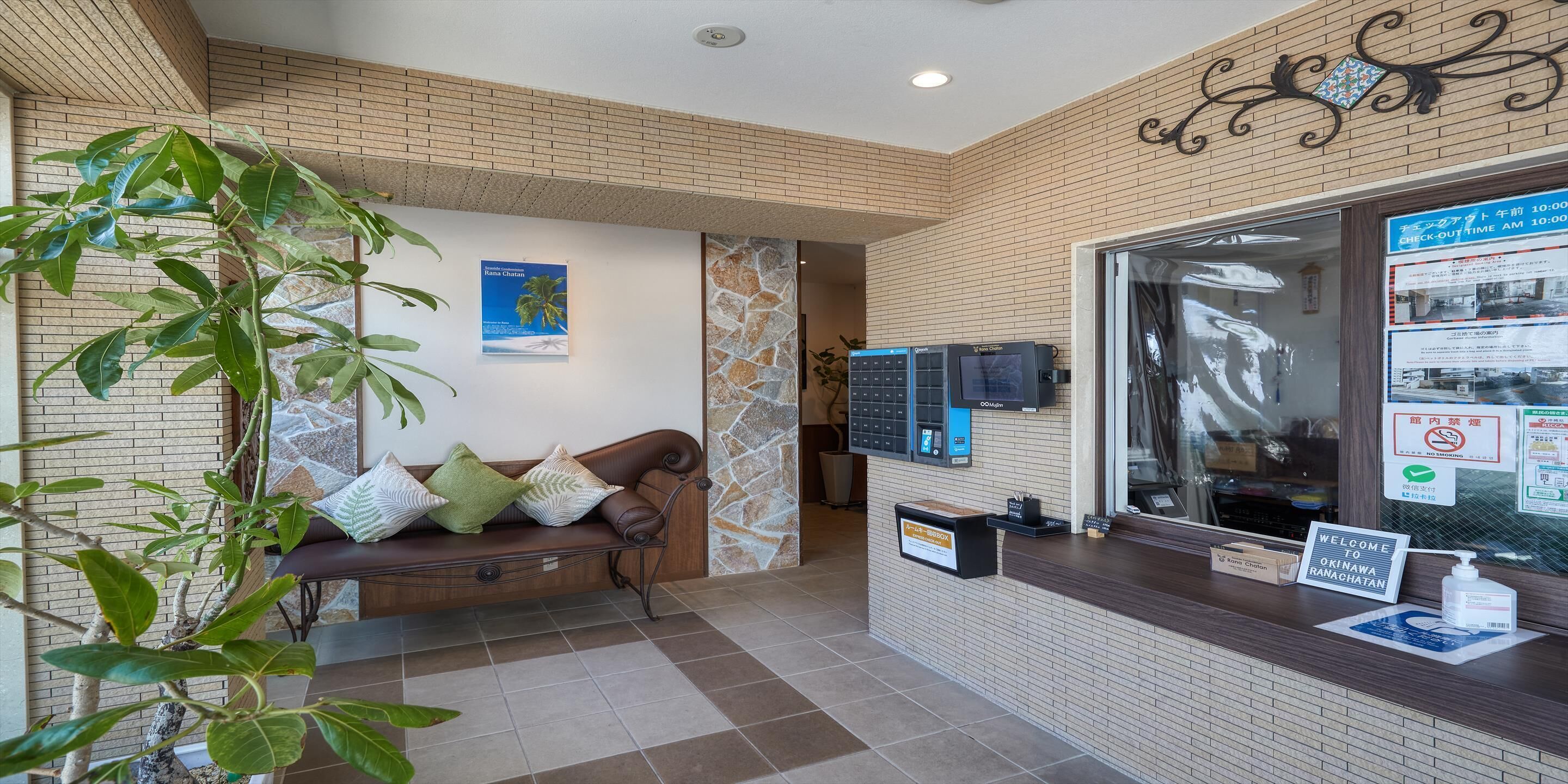 A reception area with a brick wall, a wooden bench, a plant, and a check-in counter with a computer and a sign.