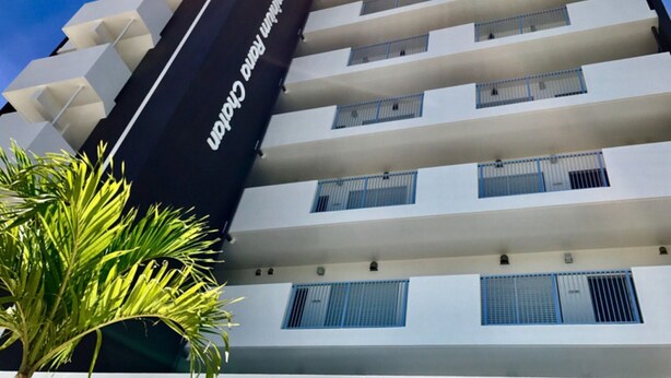 A multi-story hotel with a modern design, featuring balconies on each floor and a prominent sign on the side. - Seaside Condominium Rana Chatan (Chatan)