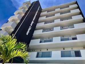 Un hotel de varios pisos con un diseño moderno, que cuenta con balcones en cada planta y un cartel llamativo en el lateral.