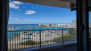 A balcony with a view of a marina, boats, and buildings across the water. - Seaside Condominium Rana Chatan (Chatan)