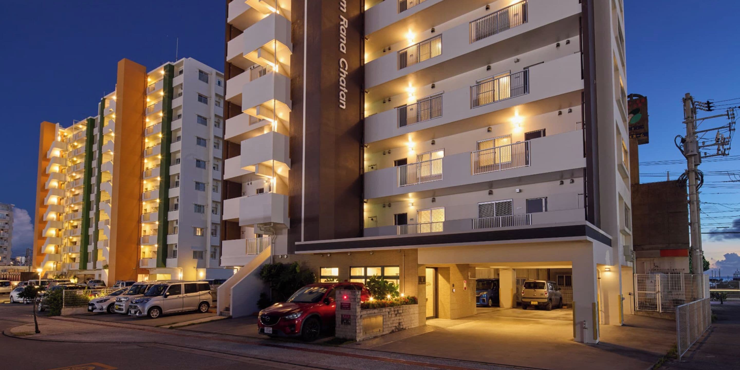 A multi-story hotel with balconies, a parking area, and a well-lit entrance.