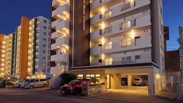 A multi-story hotel with balconies, a parking area, and a well-lit entrance.