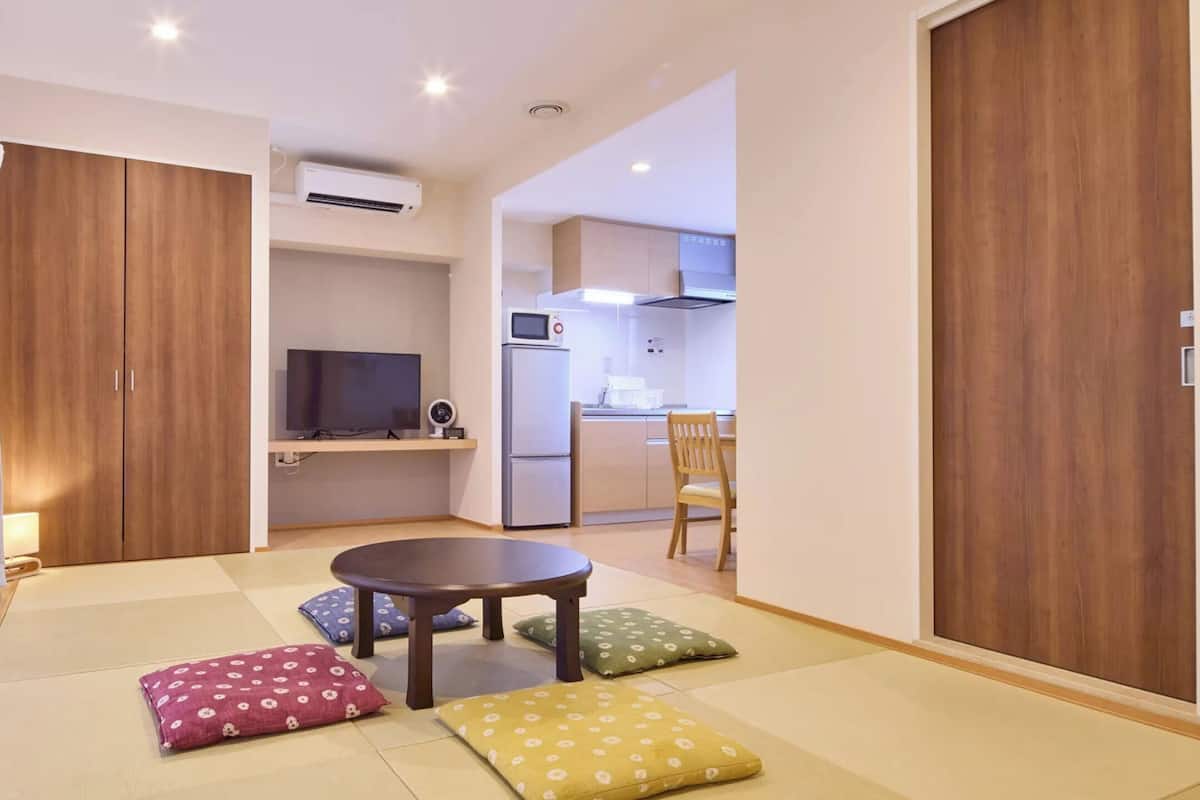 A compact living space with a tatami mat floor, a small round table, and a television in the background.