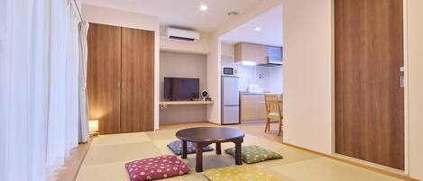 Un espacio habitable compacto con suelo de esteras tatami, una pequeña mesa redonda y un televisor al fondo.