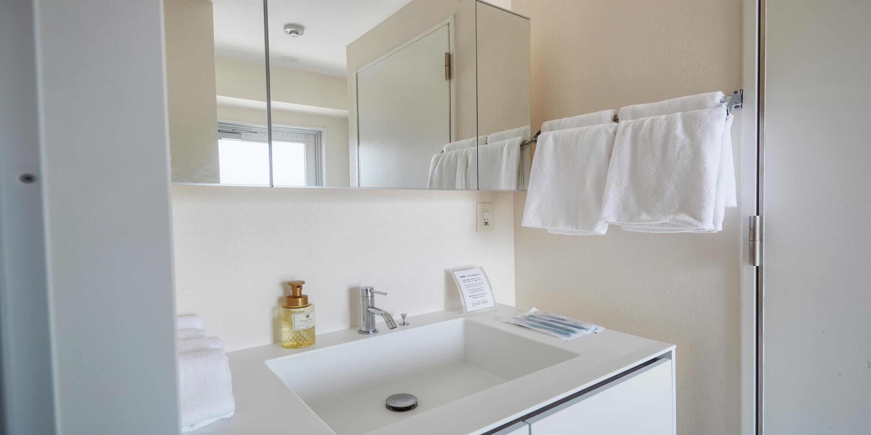 A bathroom with a white sink, a mirror, a towel rack with towels, and a bottle of soap.