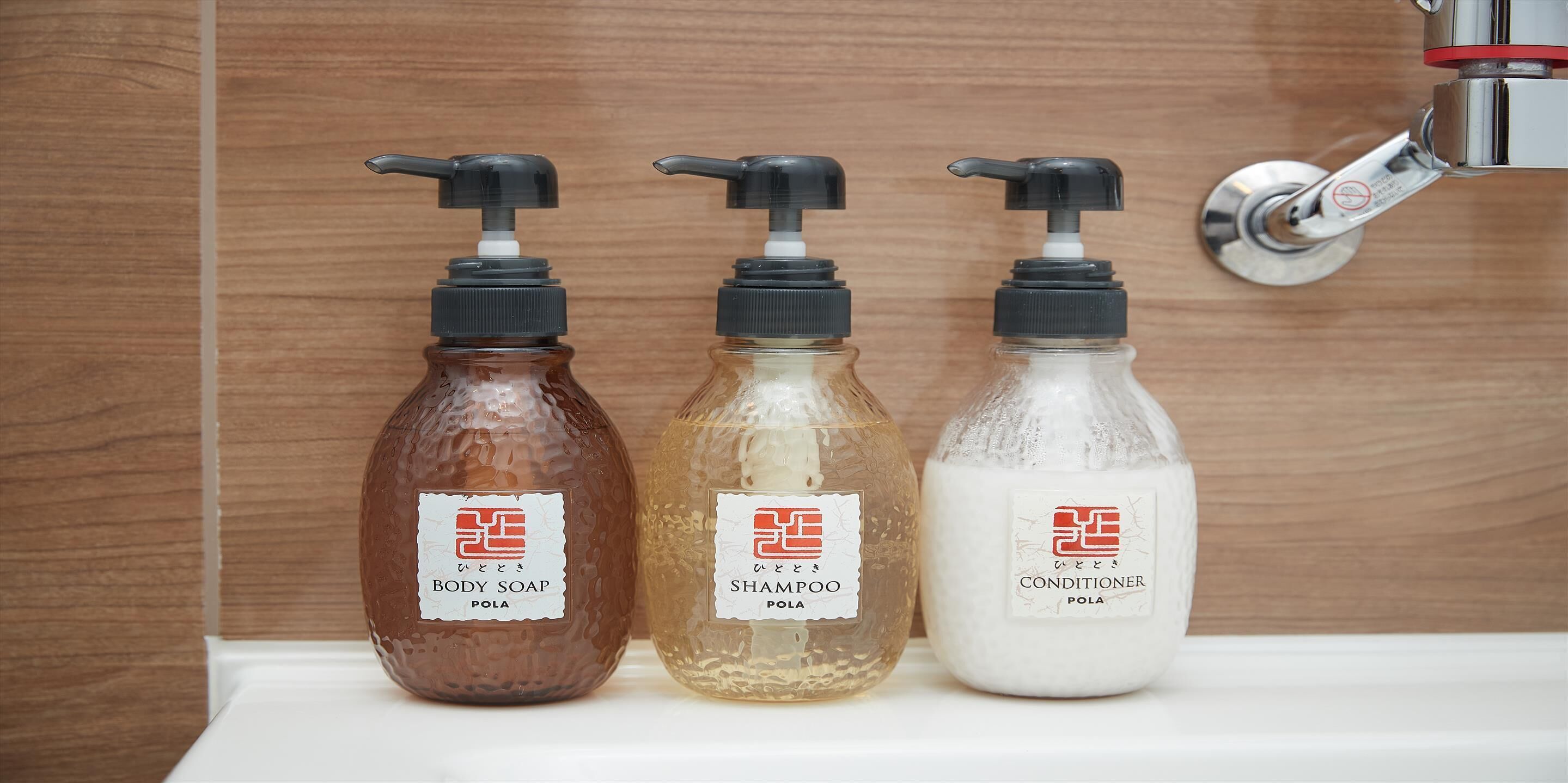 Three bottles of body soap, shampoo, and conditioner on a white surface.