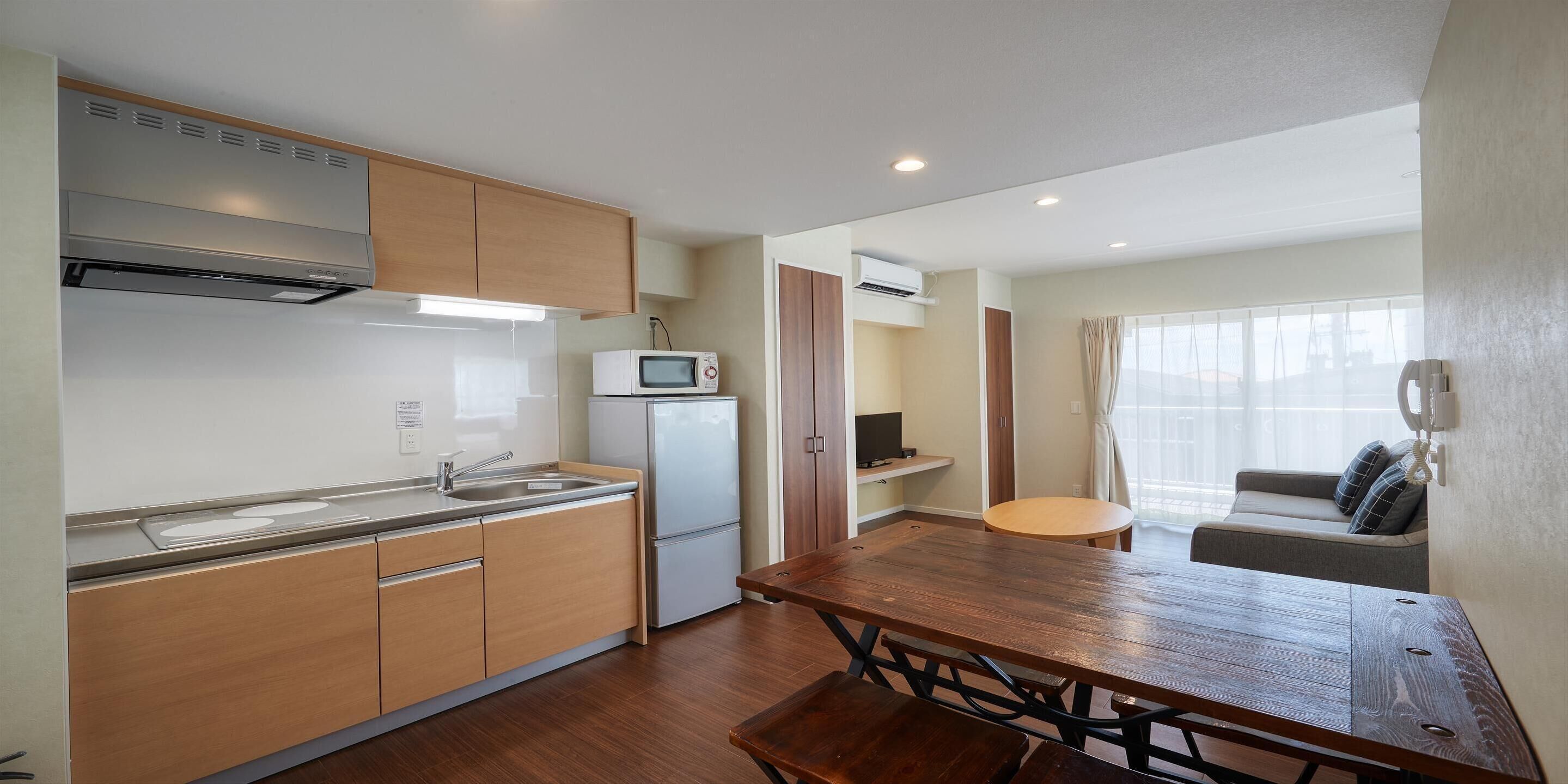 A compact kitchen with a microwave, a sink, and wooden cabinets. There is a dining table with benches in the center.