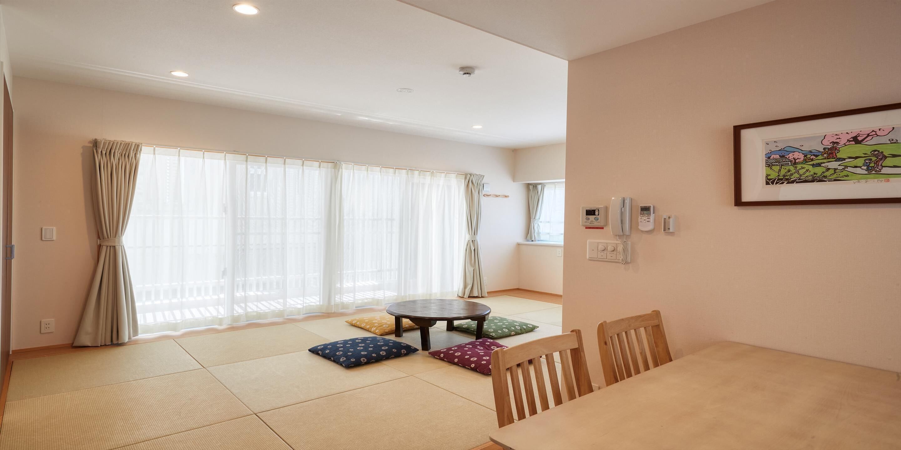 A room with tatami mats, a round table, wooden chairs, and a futon bed.