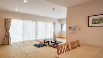 A room with tatami mats, a round table, wooden chairs, and a futon bed.
