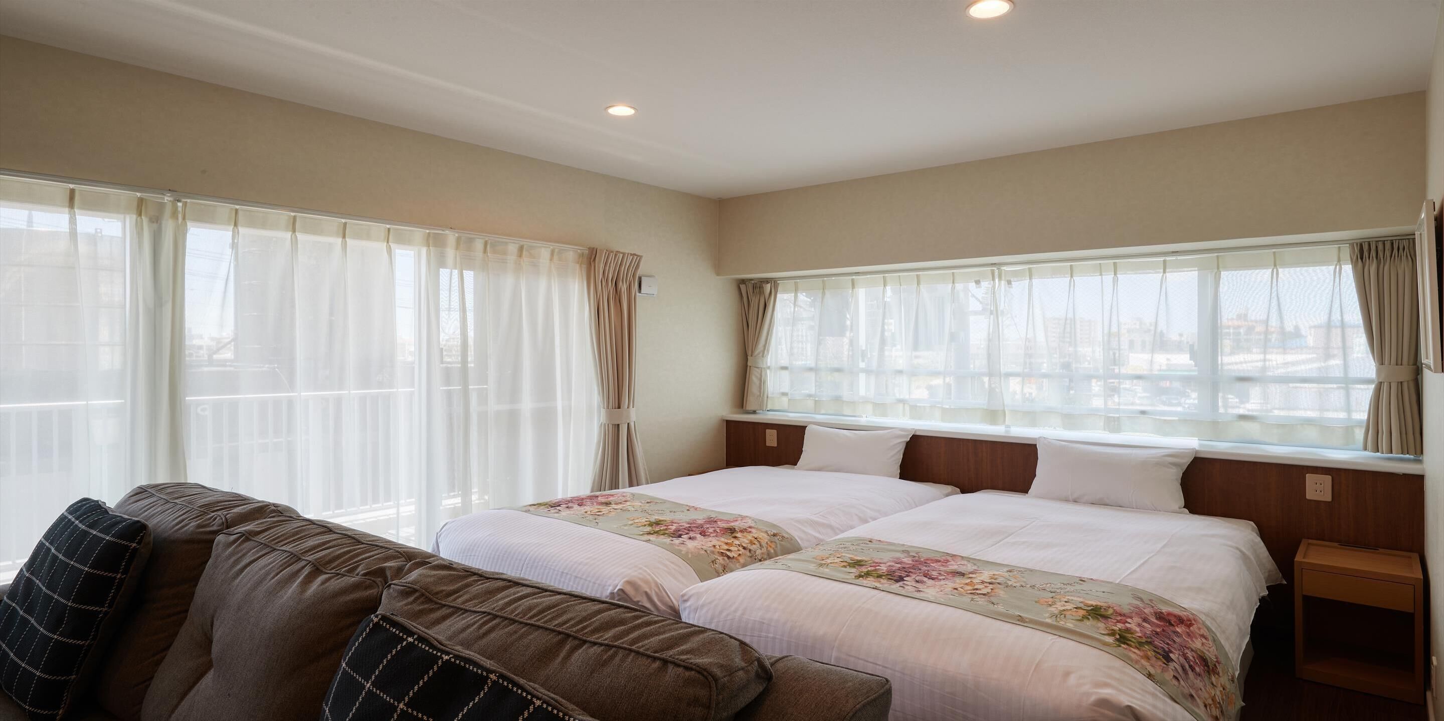 Habitación de hotel con dos camas, un sofá y ventanas amplias con cortinas.