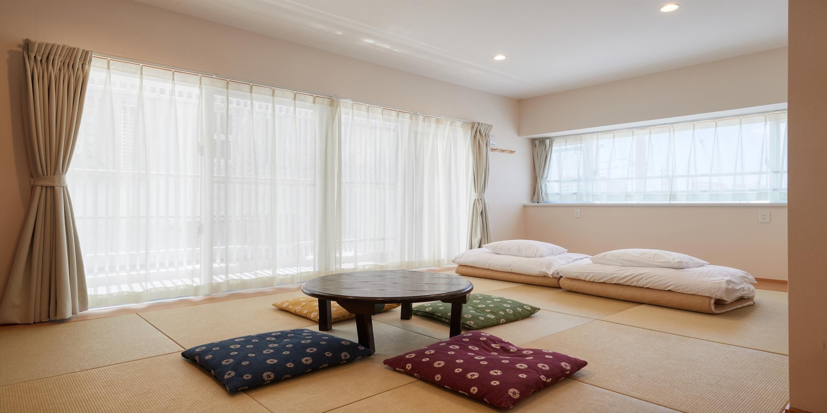 A room with tatami flooring, a low table, cushions, and a futon bed.
