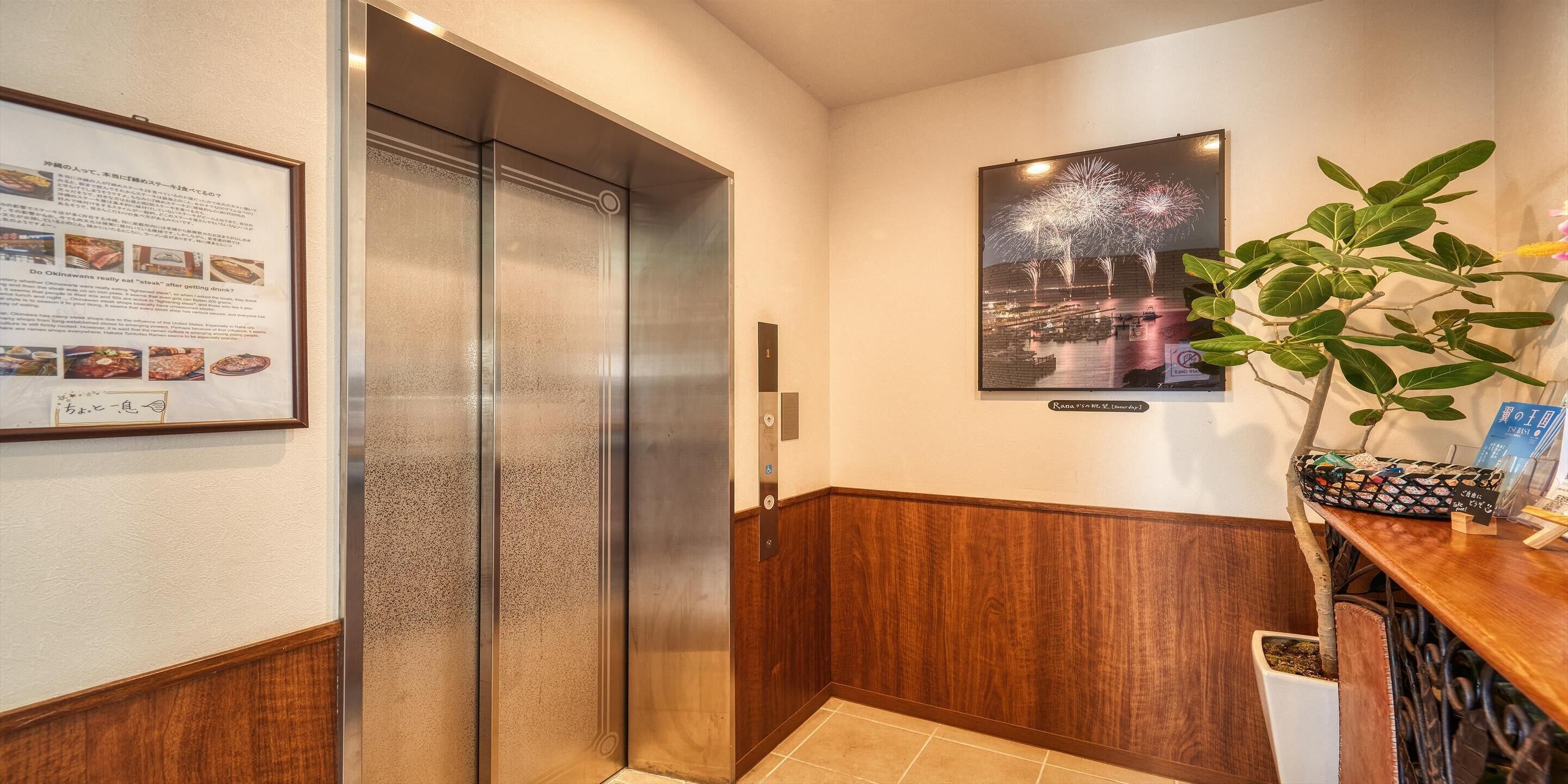 A hotel lobby with a wooden reception desk, a framed menu, and a poster of fireworks.