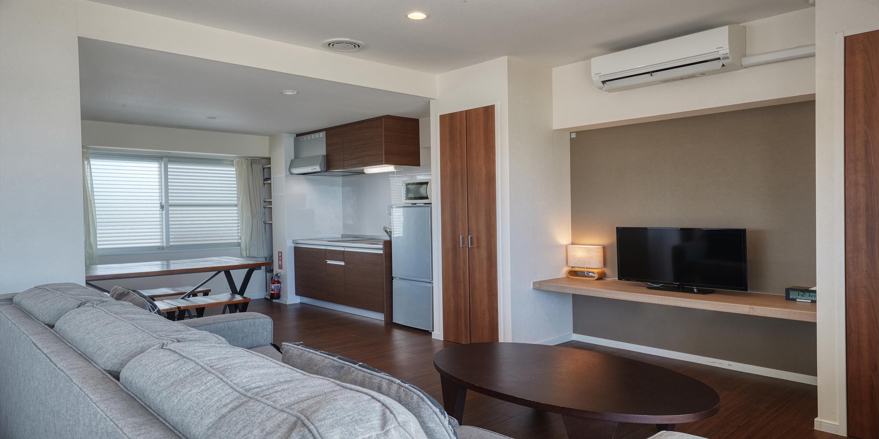 A modern living room with a sofa, a dining table, a kitchen area with cabinets and a microwave, and a TV on a stand.