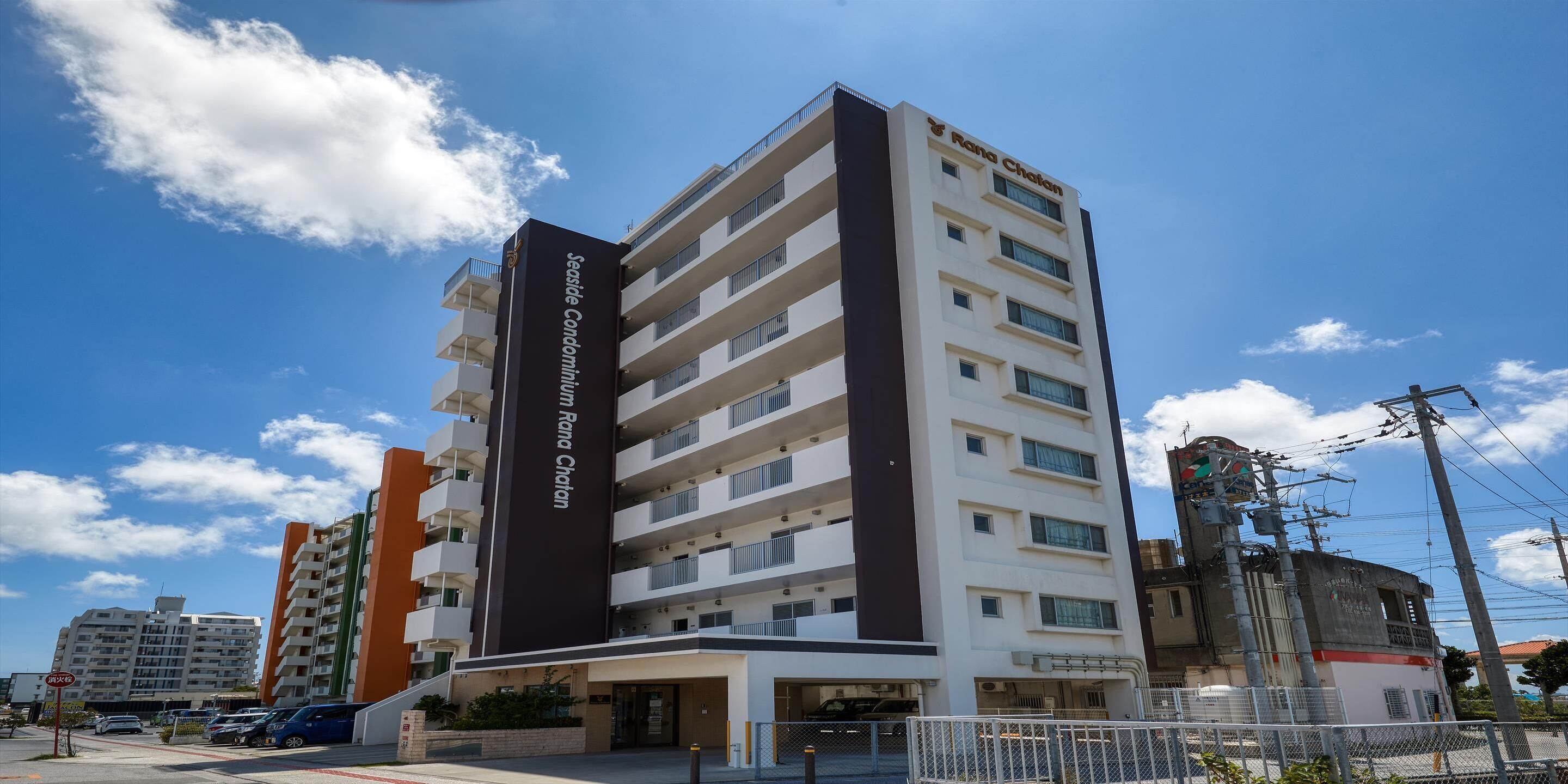 Un edificio de varios pisos con balcones, un letrero que dice "Seaside Condominium Rona Chatan" y un cielo azul despejado al fondo.