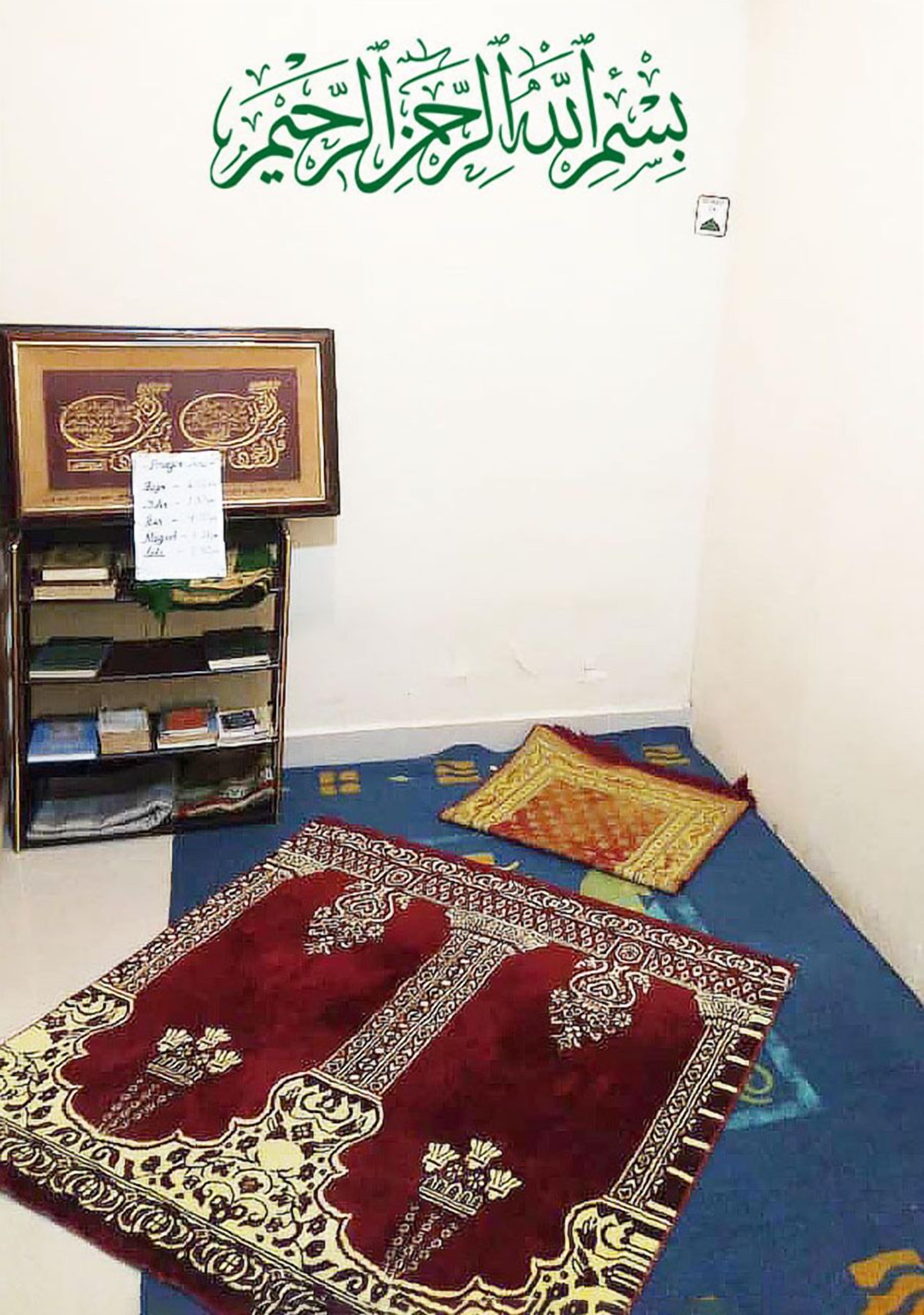 Una habitación con un tapete de oración, una estantería y un Corán enmarcado.