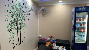 Ein Empfangsbereich mit Wandbild von Baum und Vögeln, einer Sitzecke, einem Tisch mit Blumenvase und einem mit Getränken gefüllten Kühlschrank.