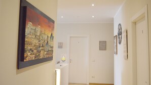 A hallway with a framed cityscape painting, a closed door, and a wall clock. - Vatican City Relais (Rome)