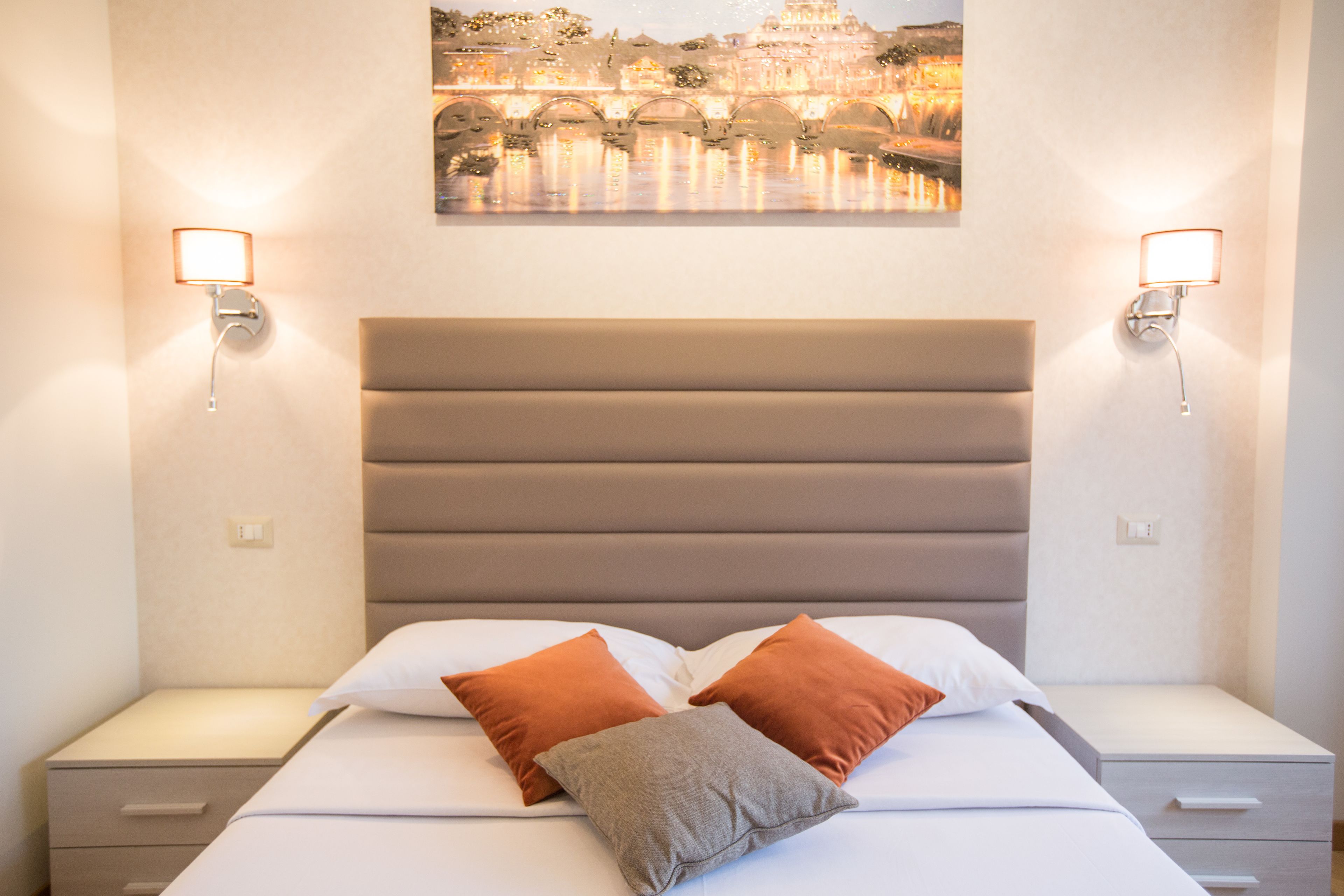 A neatly made bed with a headboard, two bedside tables, and two wall-mounted lamps.