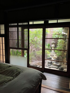A room with a bed, a window with a view of a garden, and a traditional Japanese sliding door. - Shimoza-an Kamanza-Tei (Kyoto)