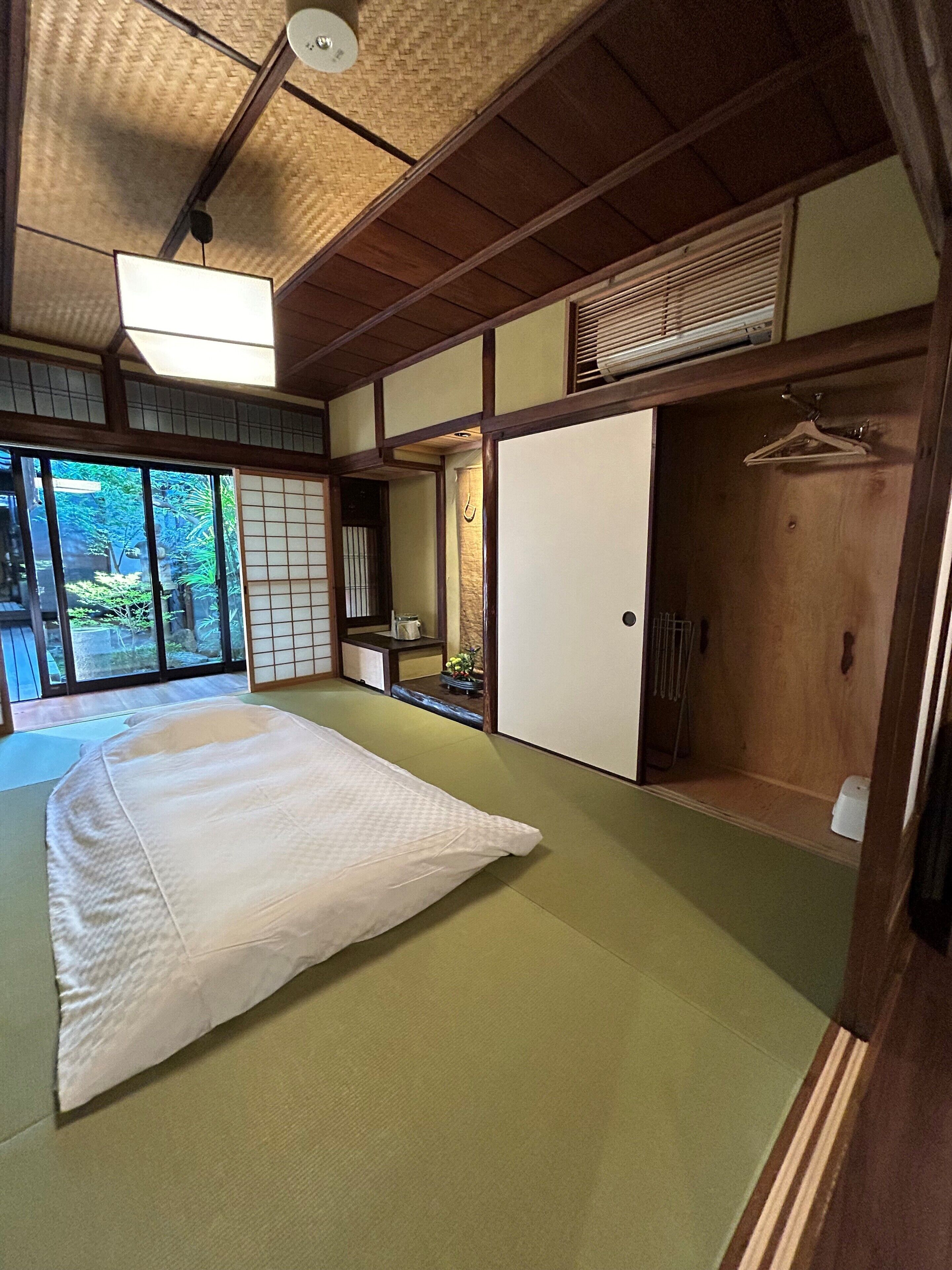 Een traditionele Japanse kamer met tatami vloeren, een groot bed, schuifdeuren en uitzicht op groen buiten.