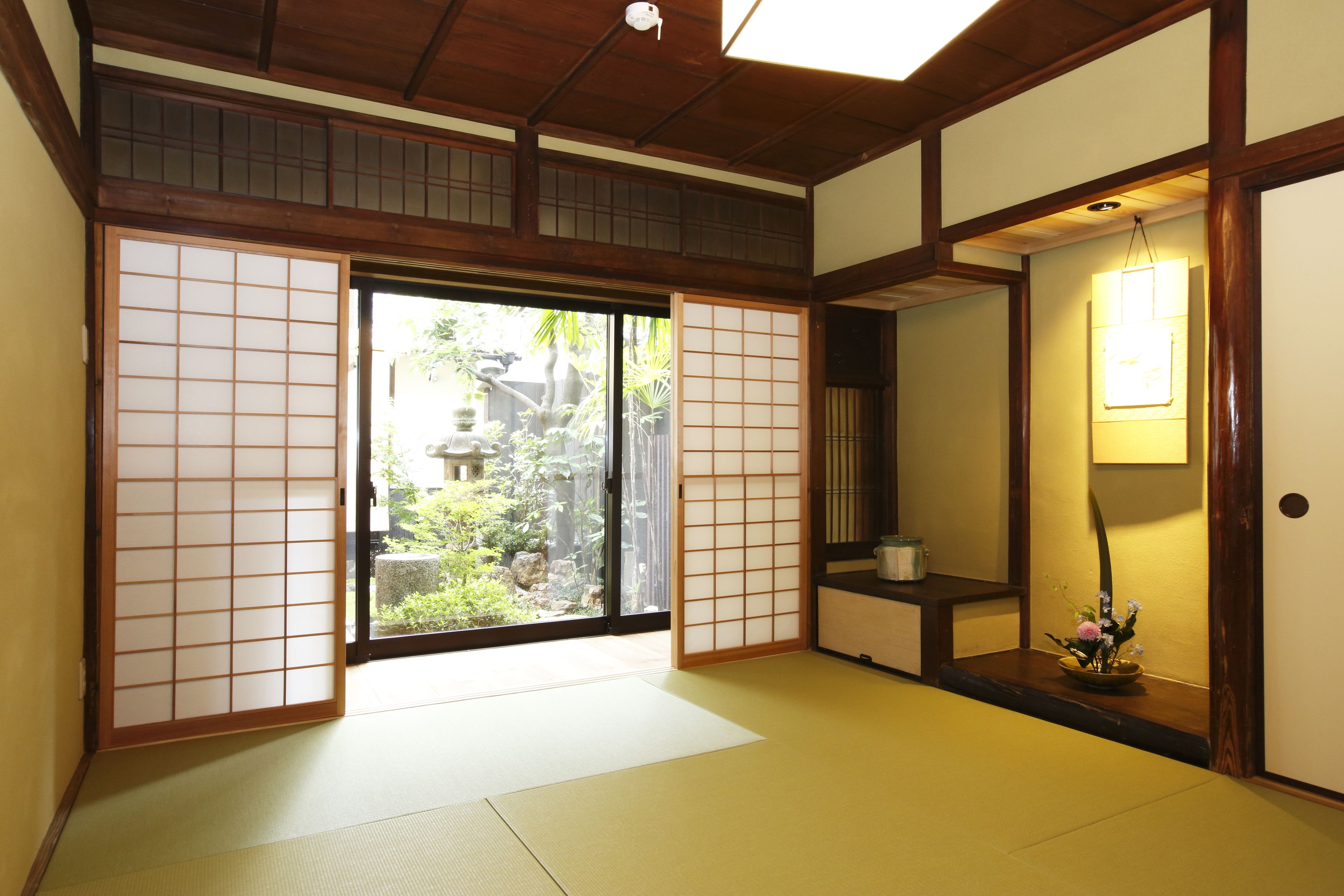 Una habitación japonesa tradicional con suelo de tatami, puertas correderas y vistas a un jardín.