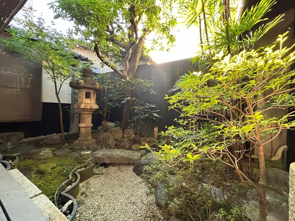 A traditional Japanese garden with a stone lantern, rock formations, and various plants. - Miyaki-tei (Kyoto)