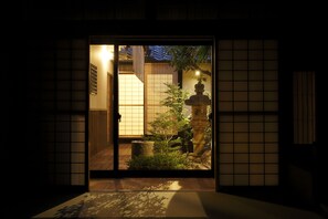 A traditional Japanese room with tatami flooring, a shoji screen door, and a small garden area with a stone lantern and plants. - Miyaki-tei (Kyoto)