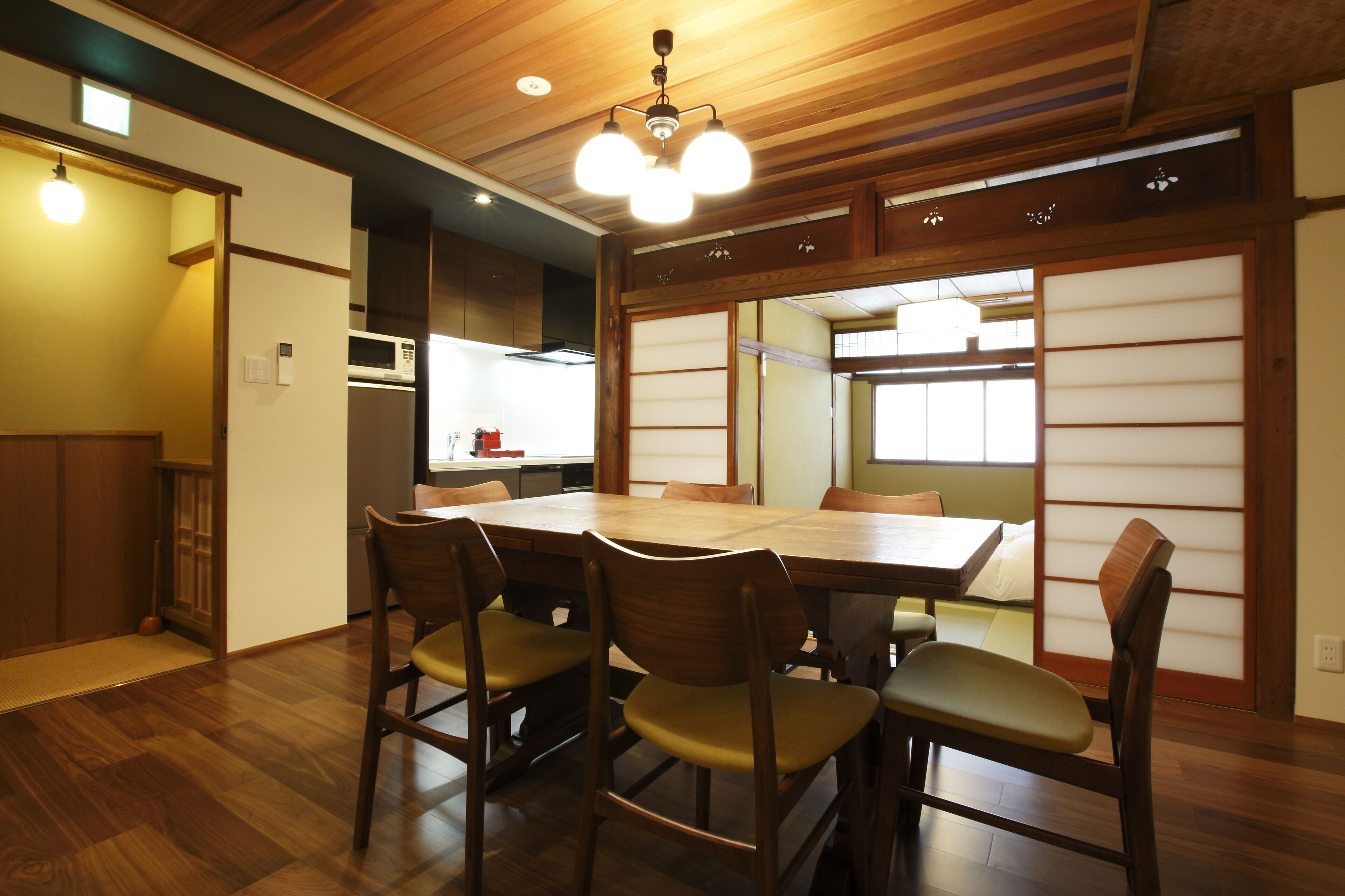 A traditional Japanese-style dining room with a wooden table and chairs, a ceiling light fixture, and sliding shoji screens.