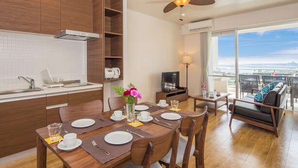 A modern kitchen with wooden cabinets, a dining table set for four, and a balcony with a view. - Private Villa Gushikumui by Coldio Premium (Motobu)