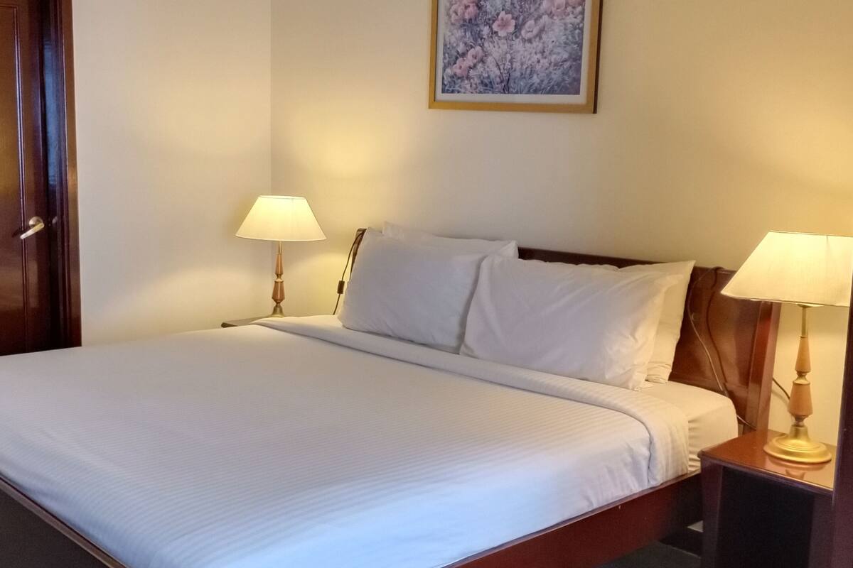 A neatly made bed with white linens, two bedside lamps, and a wooden headboard.