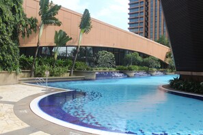 A swimming pool with a curved edge, surrounded by lush greenery and a modern building with large windows. - Best Apartment at Times Square (Kuala Lumpur)