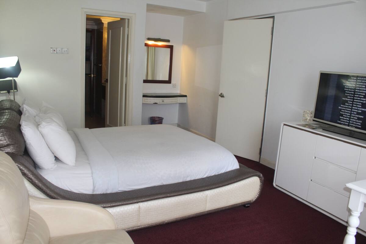 A hotel room with a bed, a television on a cabinet, a mirror, and a door leading to another room.