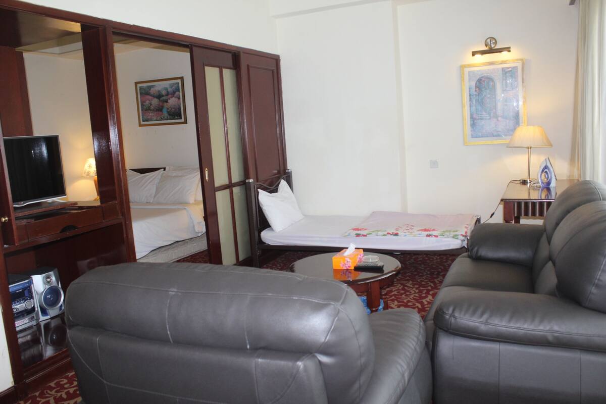 A hotel room with a bed, a sofa, a TV, and a small table with a remote control.