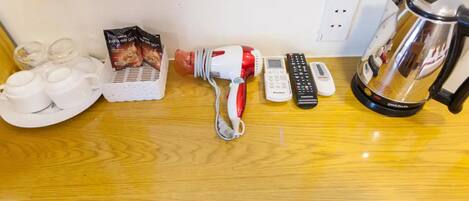 A wooden counter with a coffee maker, a kettle, a remote control, a phone, and a coffee pod package.