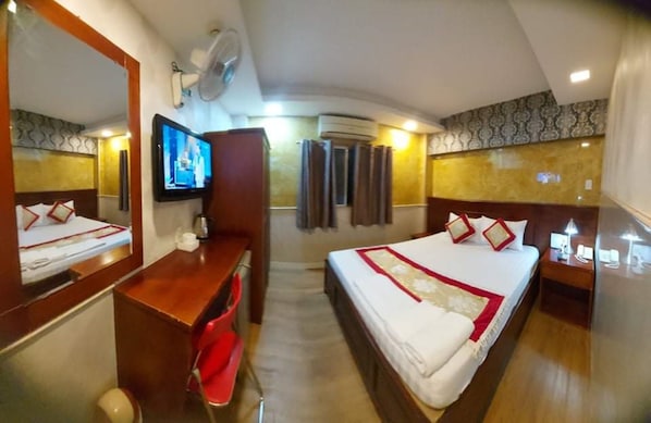 Una habitación de hotel con cama, escritorio, televisor, espejo y ventilador de techo.