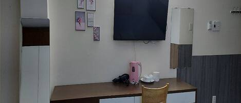 Une chambre d’hôtel équipée d’un bureau, d’une chaise, d’un téléviseur à écran plat fixé au mur, d’une petite armoire et de quelques tableaux encadrés accrochés au mur.