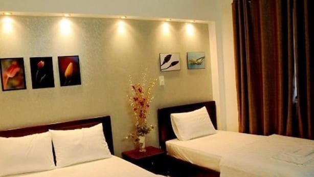 A hotel room with two single beds, a nightstand, a vase with flowers, and three framed pictures on the wall. - Ailen Garden II Hotel (Ho Chi Minh City)