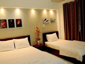 Habitación de hotel con dos camas individuales, una mesita de noche, un jarrón con flores y tres cuadros en la pared.