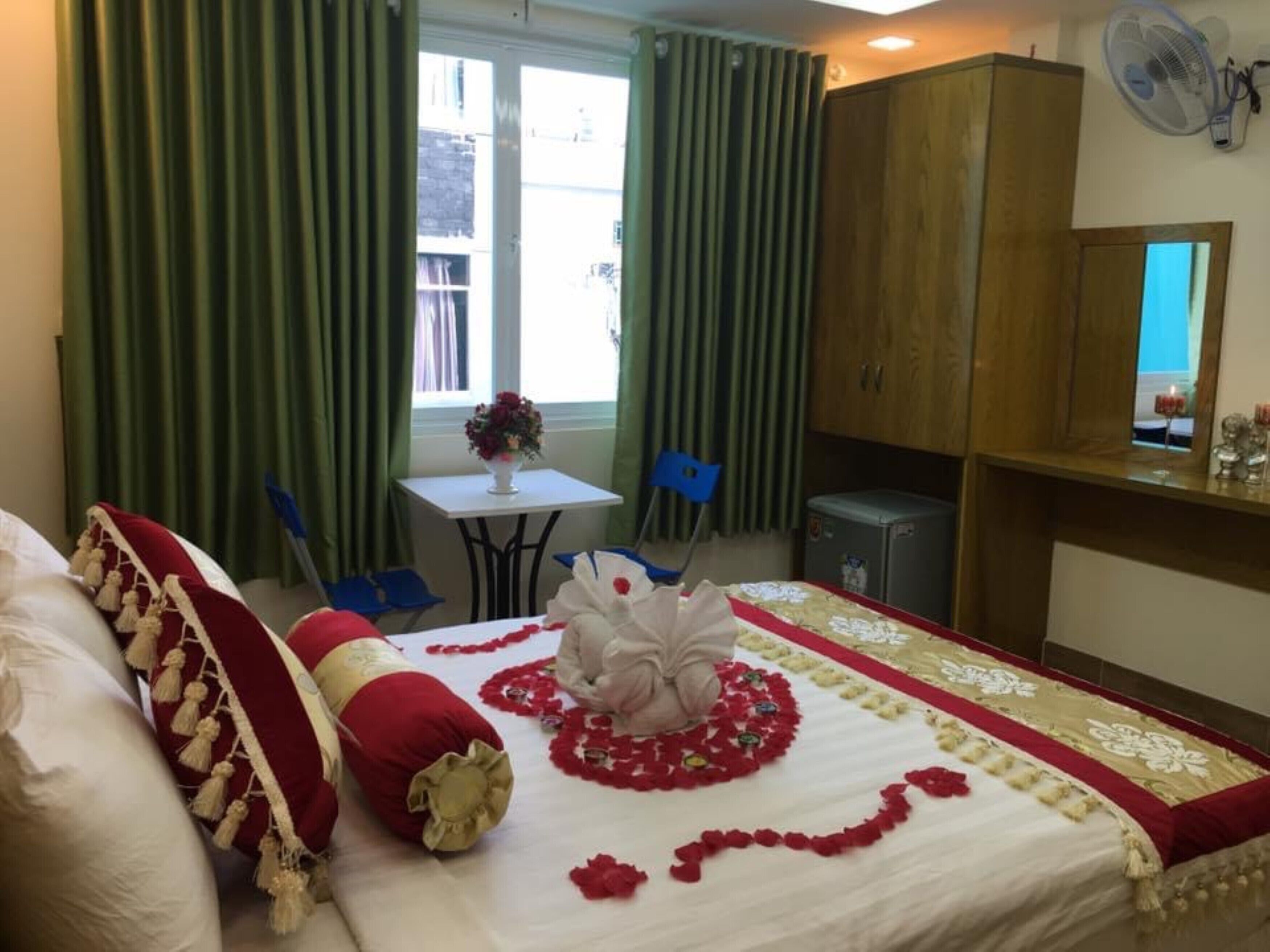 Habitación de hotel con cama, escritorio, silla, armario y una pequeña mesa con un jarrón de flores.
