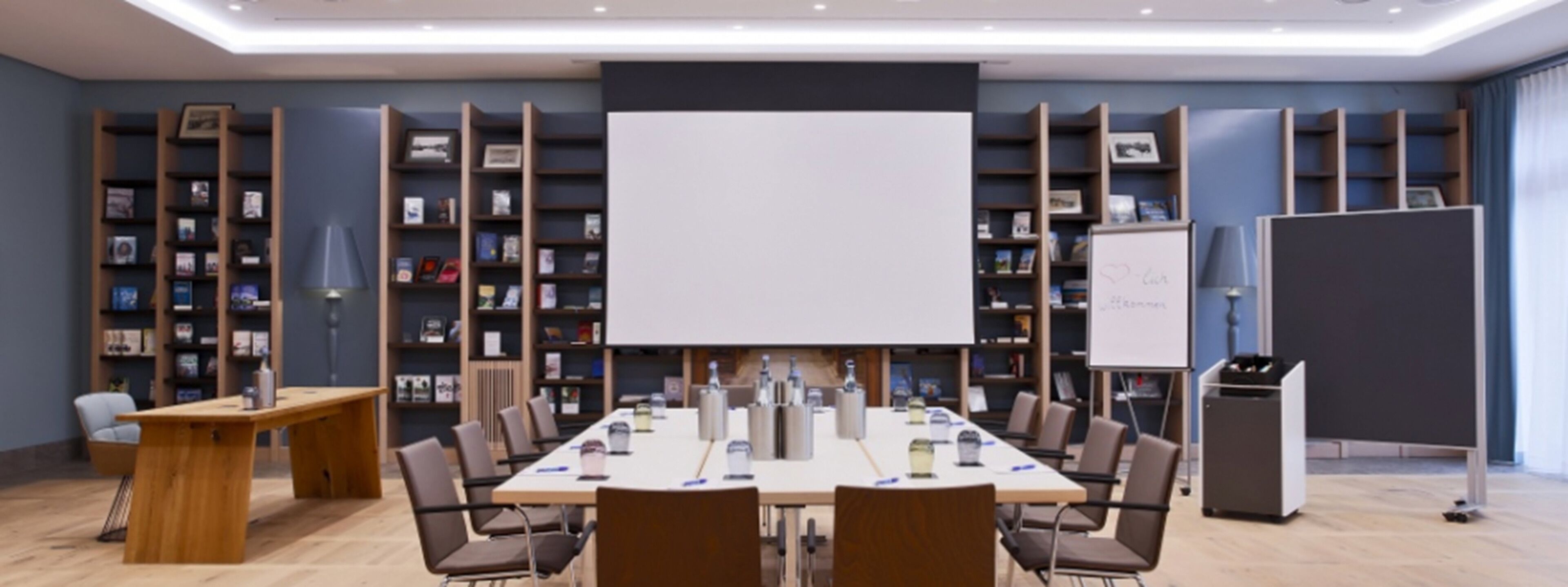 A conference room with a long table, chairs, a whiteboard, and bookshelves.