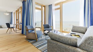 A modern living room with a large window, a sofa, two armchairs, a coffee table, and a small table with a lamp. - Upstalsboom Wyk auf Föhr (Wyk auf Foehr)