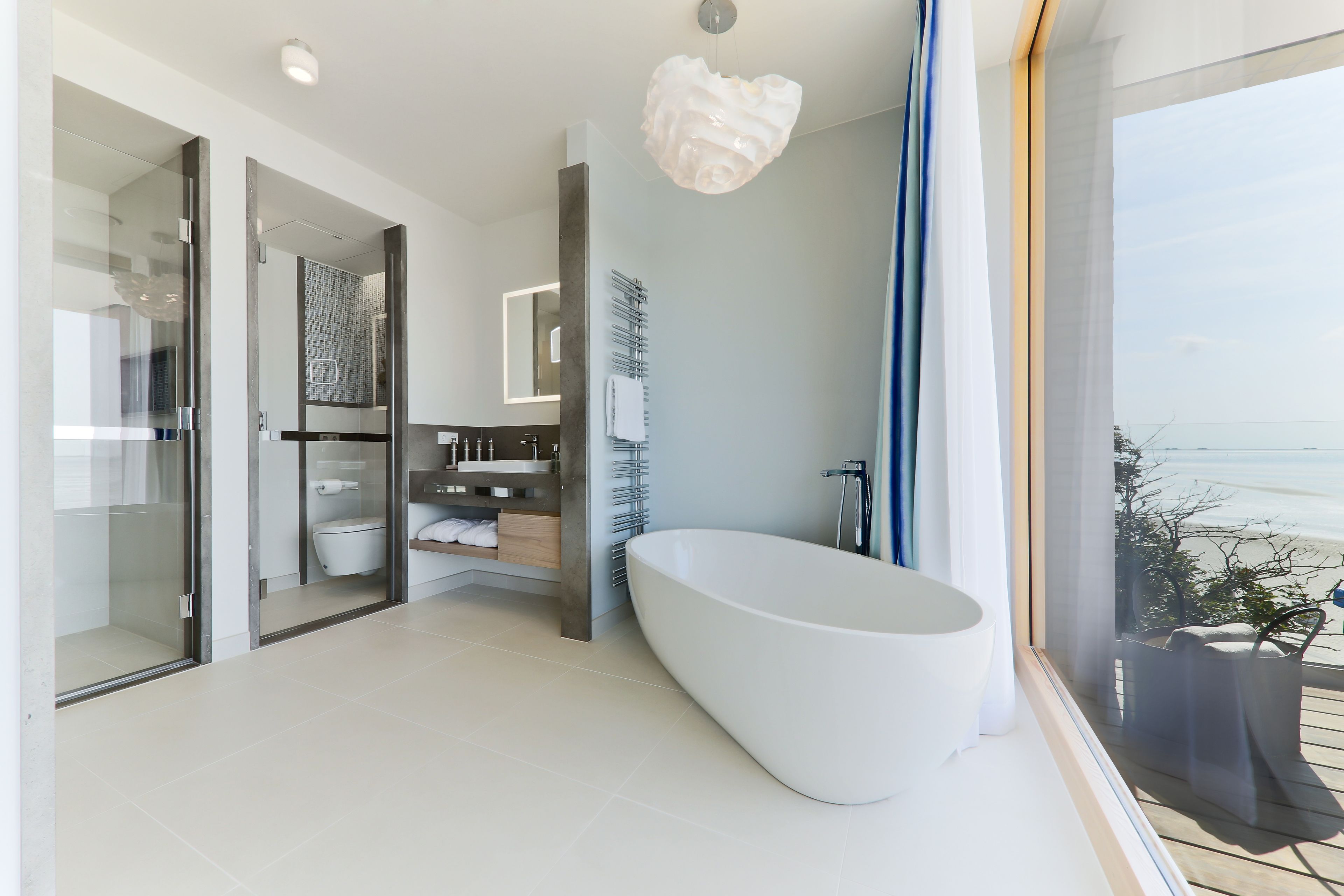 Un baño moderno con una bañera independiente, ducha con cerramiento de vidrio y vistas al mar.