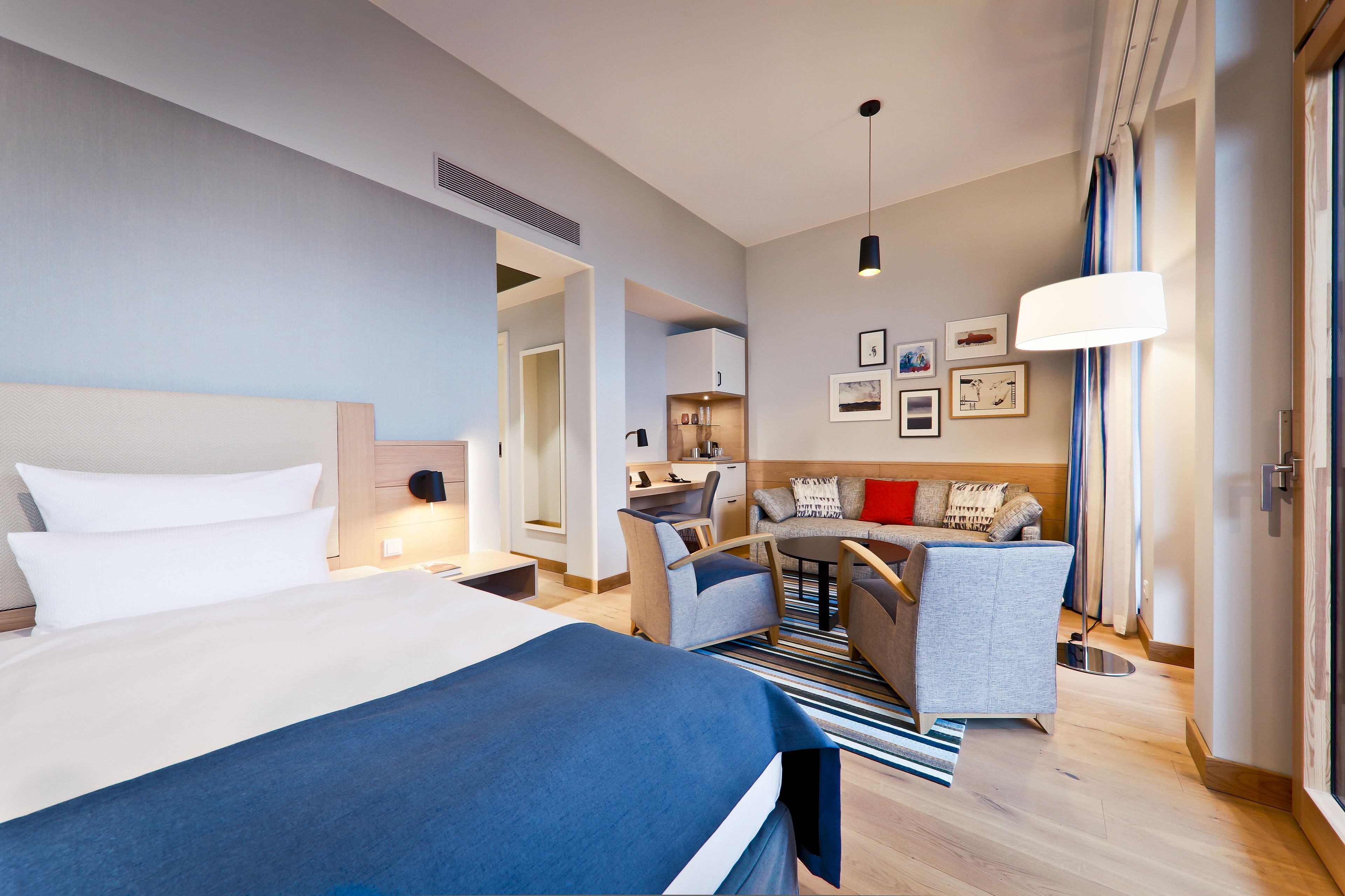 A modern hotel room with a large bed, a desk, a sofa, and a dining area.
