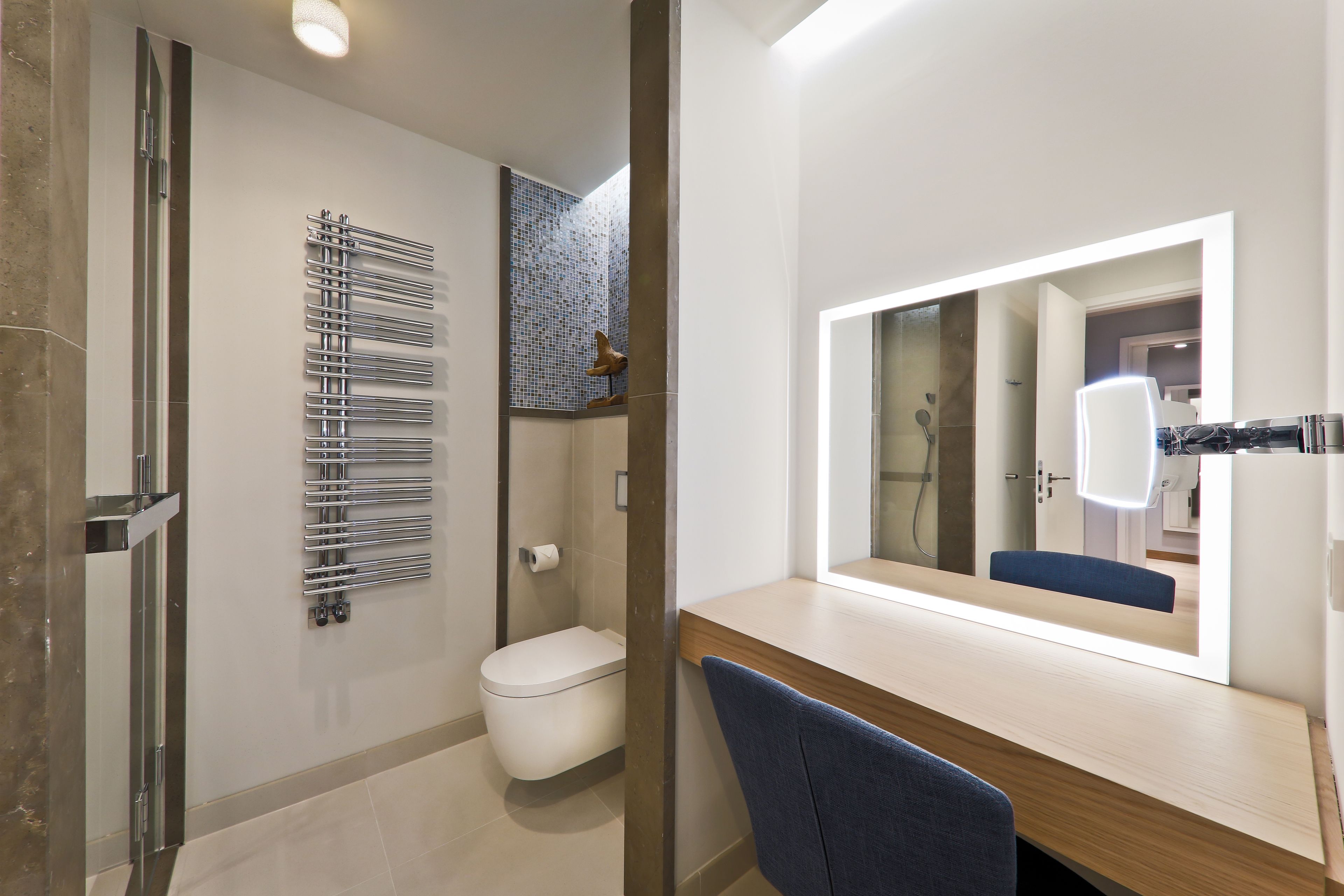A modern bathroom with a toilet, a towel rack, and a mirror with integrated lighting.